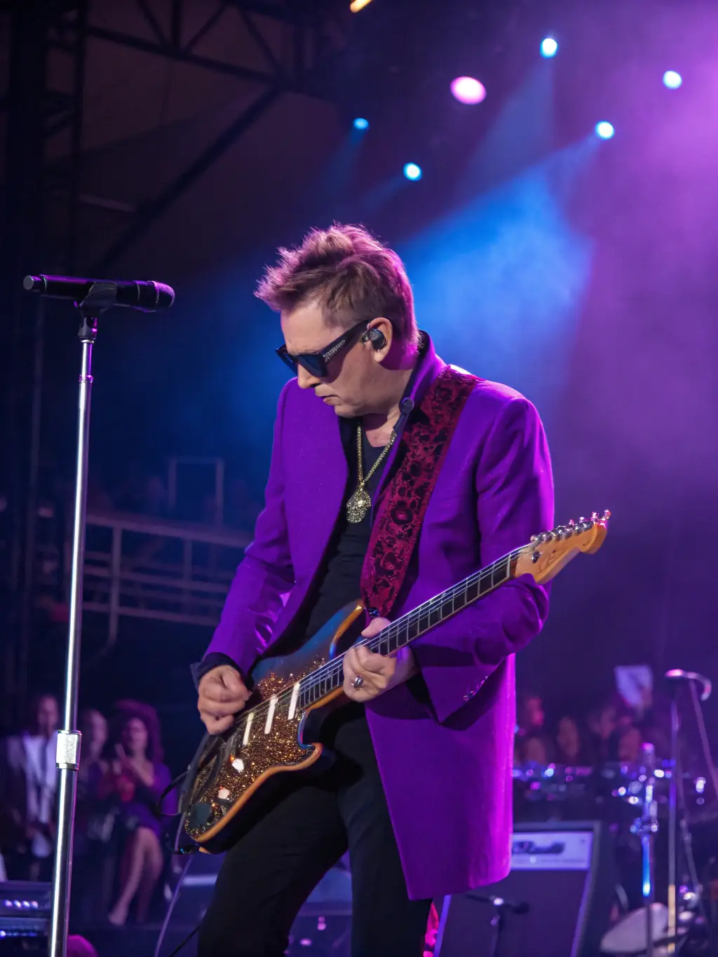 A photograph capturing a young musician passionately playing the guitar on stage during a live performance, bathed in warm stage lights, showcasing the energy and talent ARTS supports.